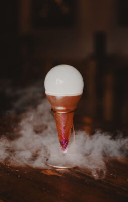 ice cream shaped glass with orange drink surrounding smoke and large smoke bubble
