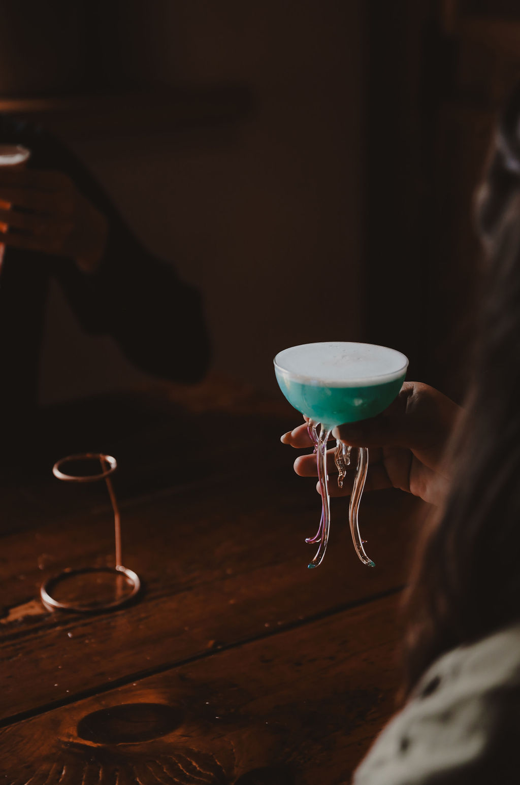 person lifting a cocktail to their mouth from a wooden table