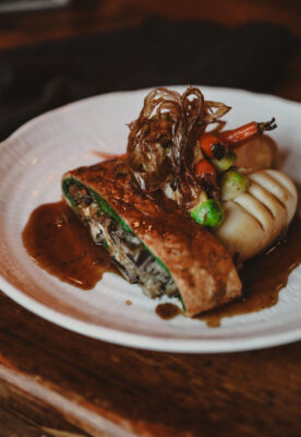 mushroom wellington wrapped in pastry on a plate with mashed potato and vegetables