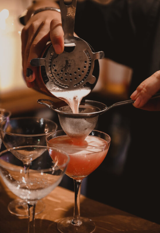 peach cocktail being poured into a mini glass with a sieve